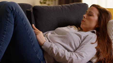 Close-Up-Of-Woman-Lying-On-Sofa-At-Home-At-Streaming-Or-Watching-Movie-Or-Show-Or-Scrolling-Internet-On-Mobile-Phone-4